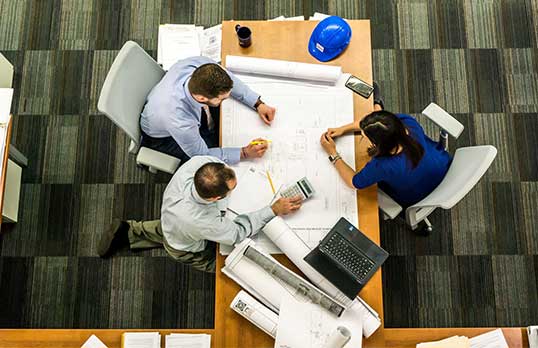 Aerial view of three adults sat around a table with a large technical drawing