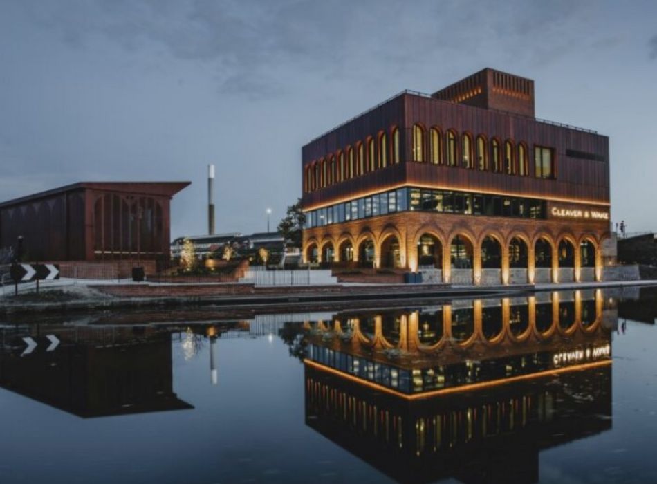 Square brick building with arched walkway by water with reflection in evening light