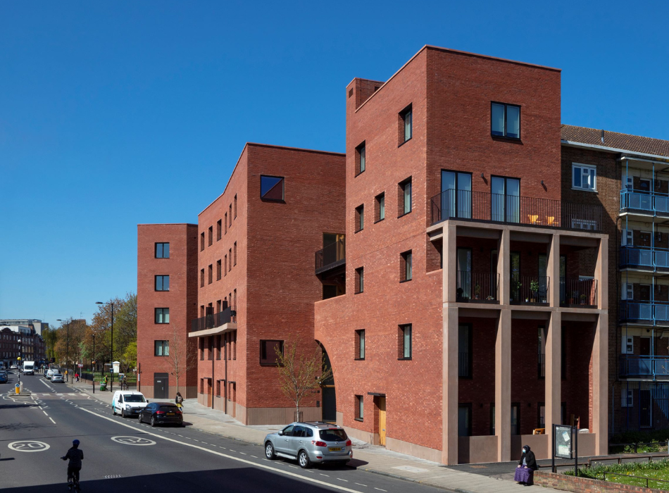 Modern red brick building with square cut out windows facing the road. Pictured in full sun with blue sky.