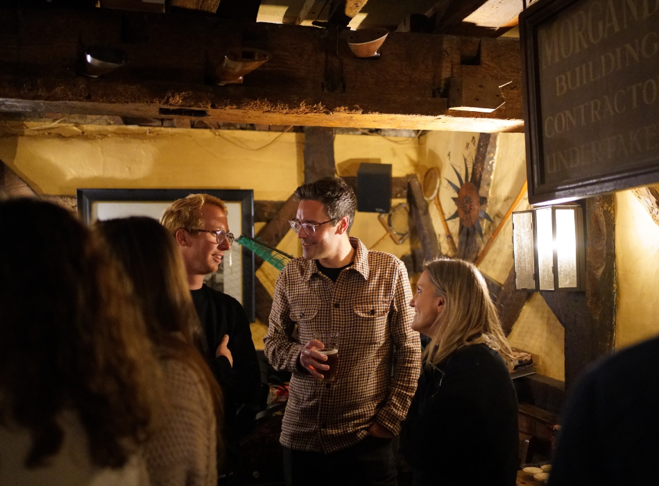 Three people talking in dimly lit bar with exposed beams and yellow walls.