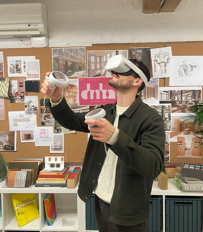 Man wearing virtual reality headset standing in front of a pinboard of ideas and pictures of architectural projects.