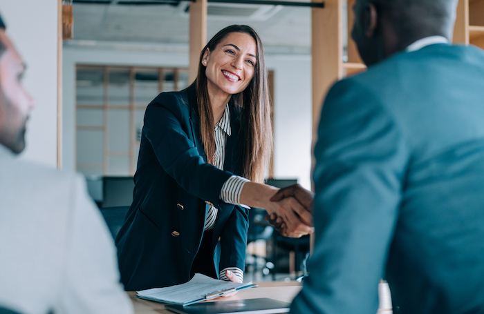 A woman in an office smiling as she shakes hands with another personjpg