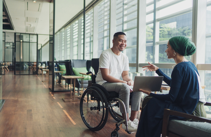Inclsuive Overlay Man sitting in a wheelchair chatting to a woman in a building designed by archite
