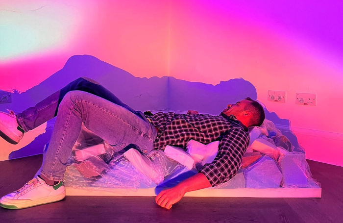 Man lying on miscellaneous foam blocks bathed in purple, pink, and orange lights