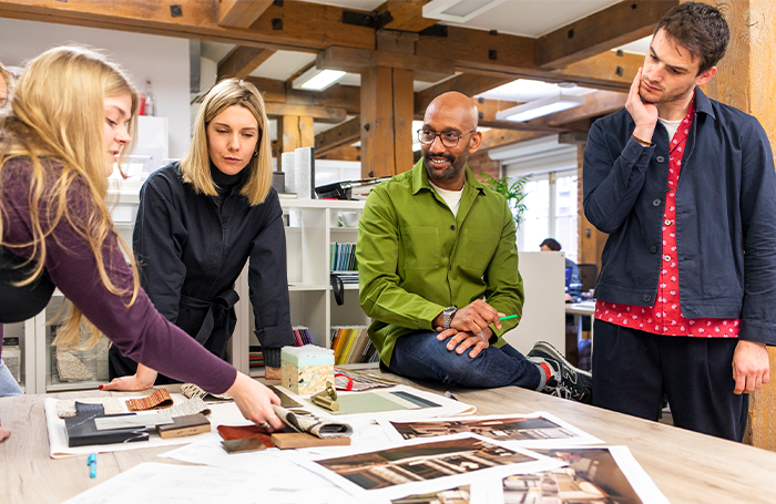 Four architects standing around a table of images discussing and smiling.