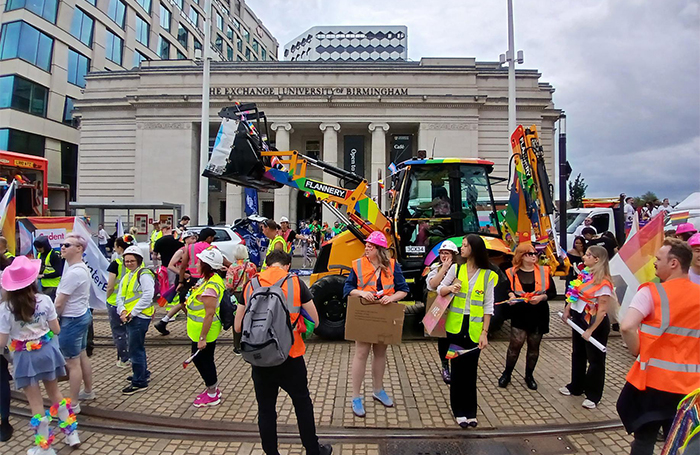 Architects in hives vests marching next to a rainbow decorated diggerjpg