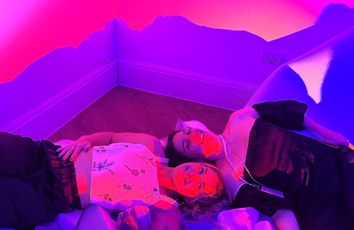 Two people lying on miscellaneous foam blocks bathed in purple, pink, and orange lights