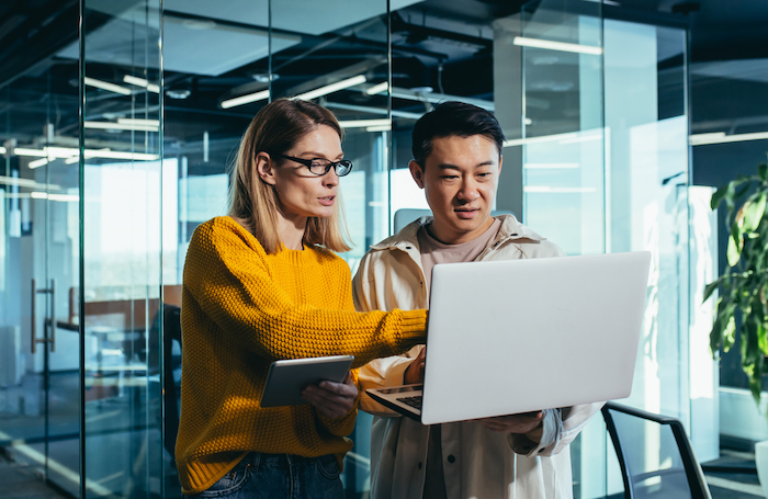 Two people in an office looking at a laptop screenjpg