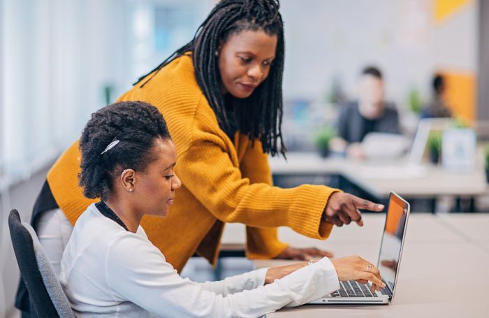 Two women in an office discussing a topic while looking at a laptopjpg