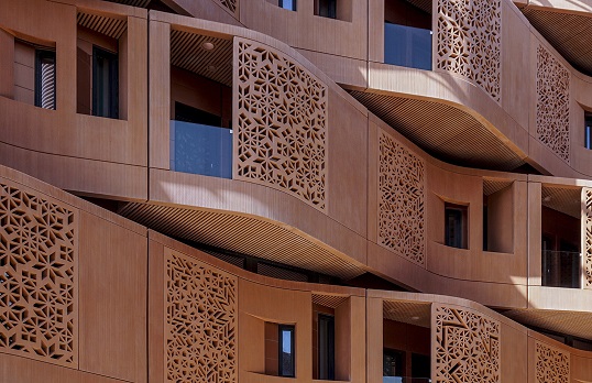 Irregular shaped terracotta coloured recessed balconies with lasercut metal facades