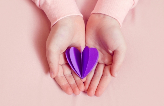 Hands on a pink background holding a purple paper heart