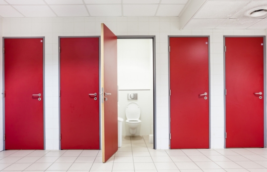 A row of closed toilet cubicles with red doors and one open