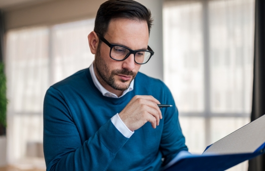 An architect in a blue sweater reading some papers at his desk