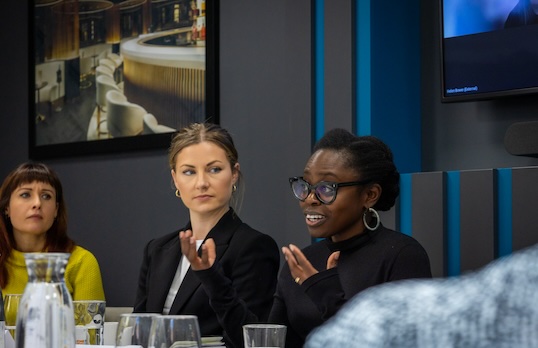 A woman speaking on a panel during an event, other women are looking towards her