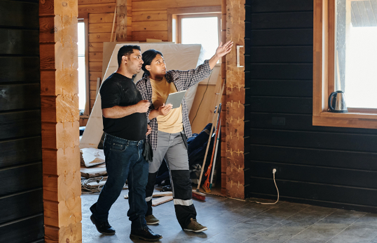 Two adults walking through a room under construction pointing and holding an iPad