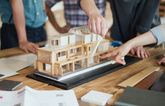 Group of architecture students looking at a model house on a table