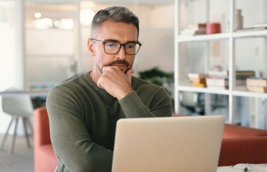 Man sitting at a desk looking at laptop in deep thought