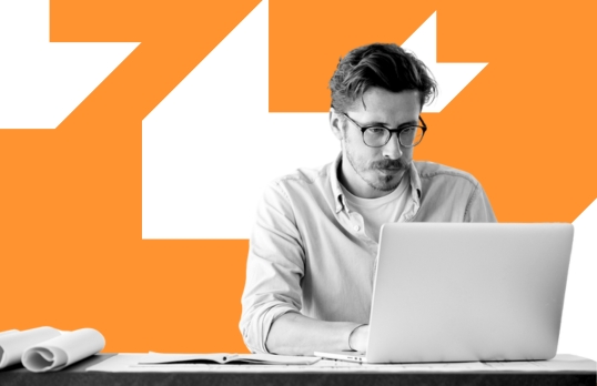 Man wearing glasses sitting behind a laptop on an orange background 