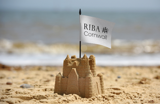 sandcastle on a beach with a white flag bearing RIBA Cornwall logo