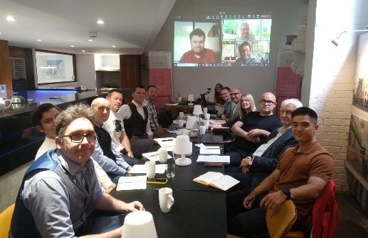 RSAW Council seated at a table with a projection of an online meeting at the back