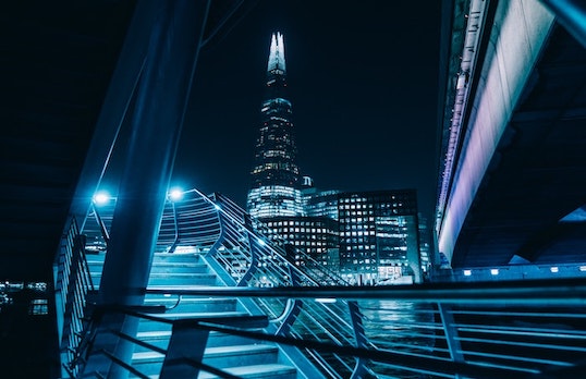 Night time view of a light up foot bridge and pointed skyscraper in the background