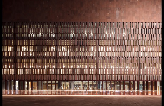 The Learning Laboratory lit up at night. A large brown tiled building, with brown sun shades partially obscuring all windows aside from the floor to ceiling ground floor windows.