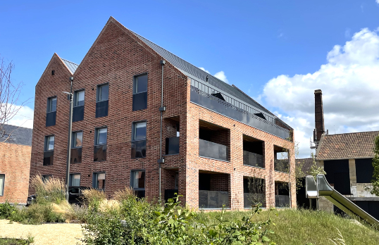 A red brick industrial building modernised with new roofing and terraces set among wildflower gardens .