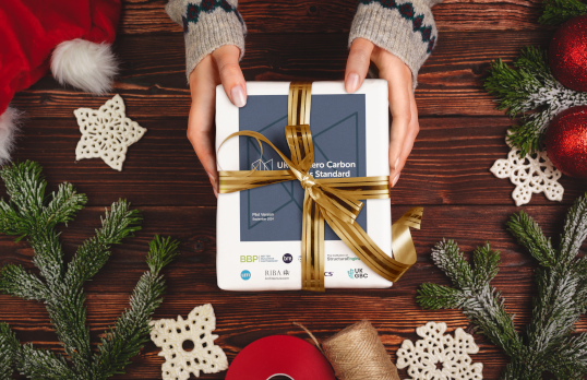 Manicured hands holding parcel wrapped in bow with various winter themed accessories scattered around the table