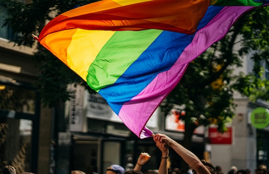 Rainbow pride flag being held high and waved by a person in the street