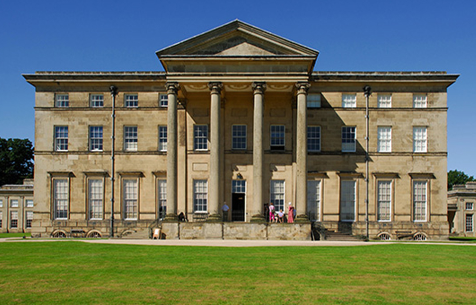 Coloured photograph of Attingham Park, a rectangular stone estate with neoclassical columns at the middle entrance and triangular detail above