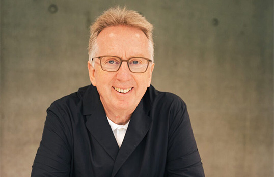 Older man with glasses and short grey hair wearing a black blazer and white tee