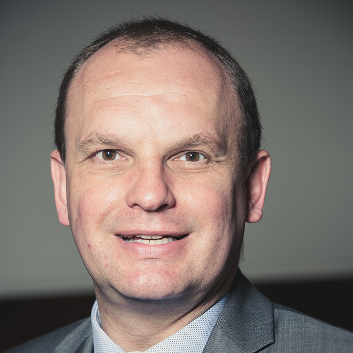 Portrait of Marek Suchocki - RIBA Stirling Prize 2023 jury member, in a grey suit smiling at the camera