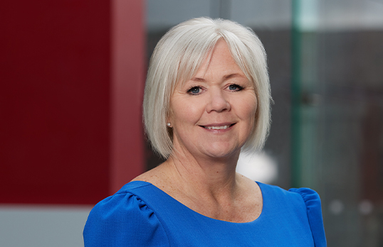 Belinda Irlam Mowbray wearing a blue top in front of the red entrance to RIBA North