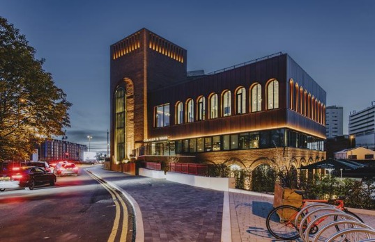 Imposing quayside modern square building with tower with arched cut out windows overlooking busy road