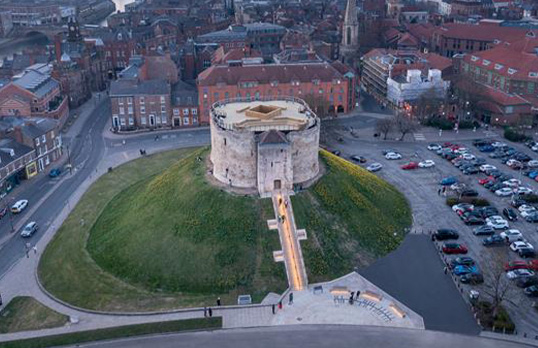 Ancient castle on grassy mound with modern city development on all four sides