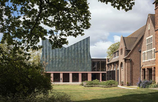Tall V-shaped roofed building with glazed tile exterior and pink concrete ground floor structure.