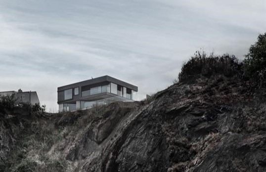 Modernist square building set back from cliff edge