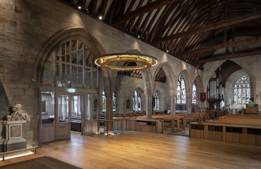 Stone built church with exposed wooden rafters and beams featuring new hanging halo light installation