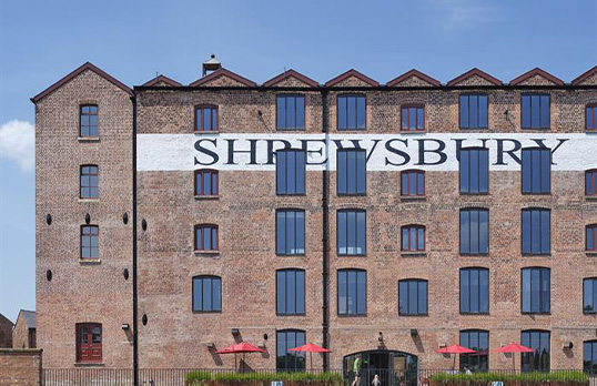 Tall multi-storey brick built industrial building with cut out windows and the word SHREWSBURY painted across at high level.