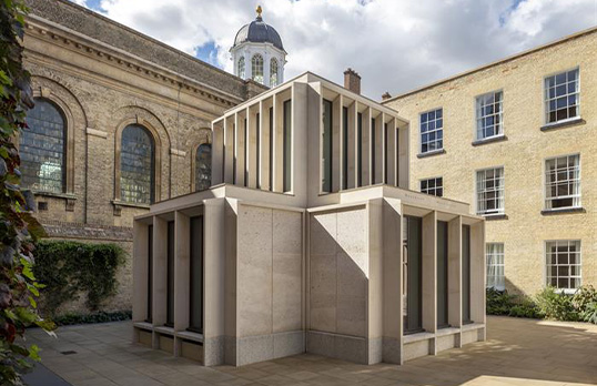 Modern cross shaped building made of Portland stone with tall thin windows set in small courtyard within college grounds.