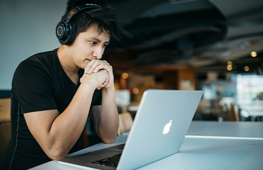 Man wearing headphones looking thoughtfully at a laptop