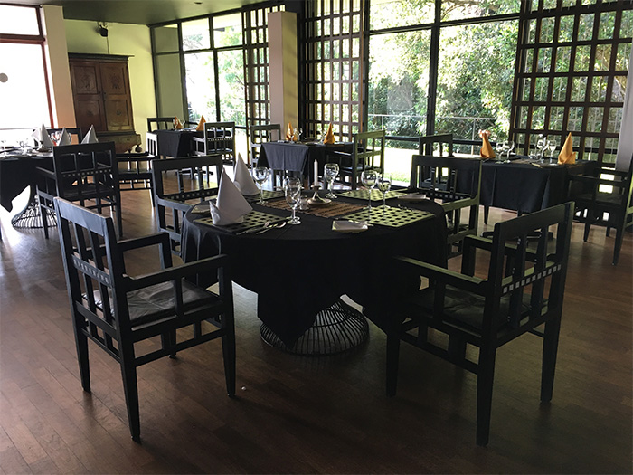 Dark wooden dining tables and chairs in an open concept dining room with greenery through the windows - Kandalama Hotel