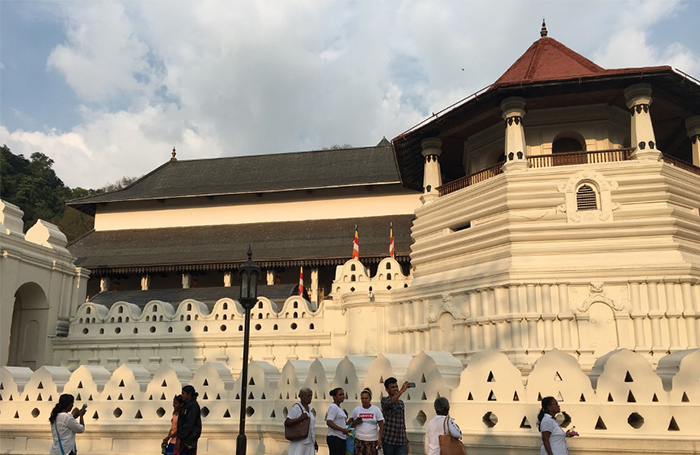 Large white decorated temple with red roof and visitors outside, Temple of the Tooth - Colombo, Sri Lanka