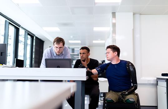 Man in wheelchair looking at computer with fellow workers 