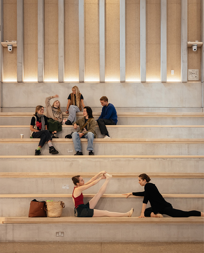 Group of students and ballet dancers sitting on bleachers in a well lit room
