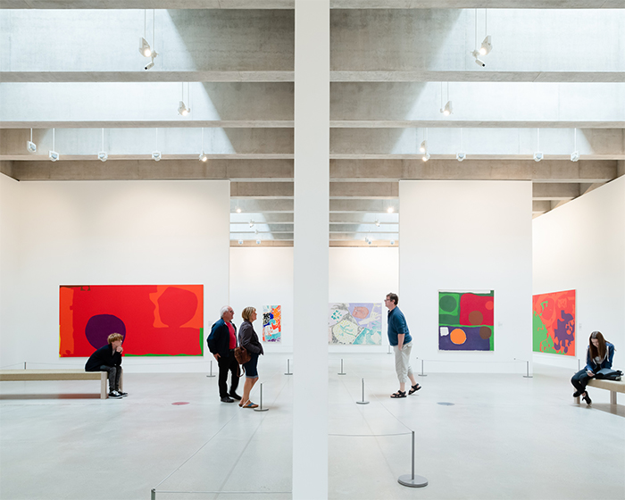 Adults walking around a tall white gallery with colourful abstract paintings on the walls