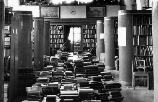 Black and white photograph of the RIBA Library with books on art deco shelves and stacked along the middle floor
