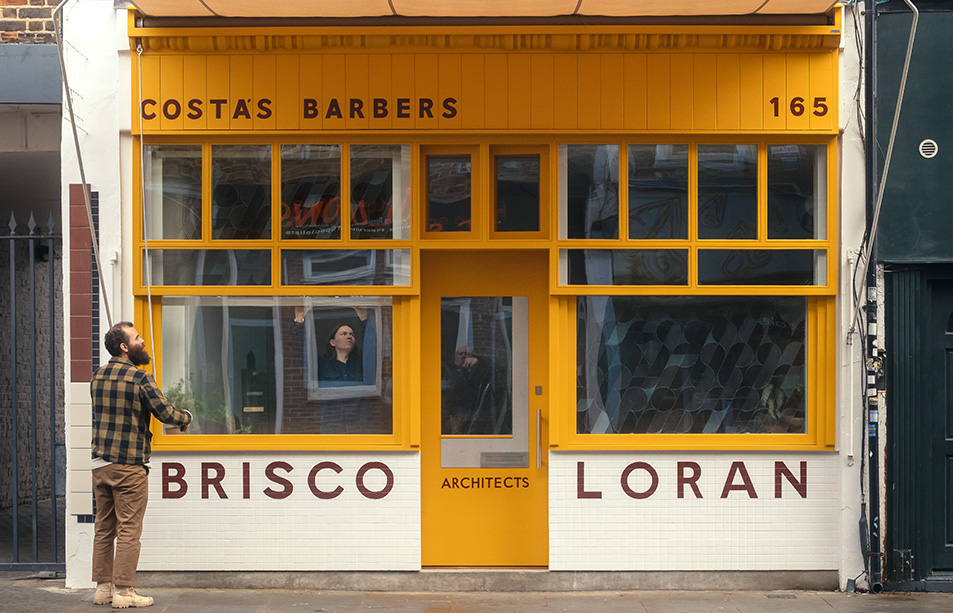 Yellow shopfront of Costas Barbers with people in the window