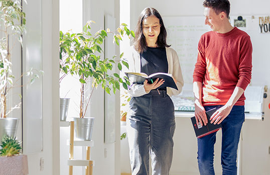 Two adults with books walking down a sunny corridor 