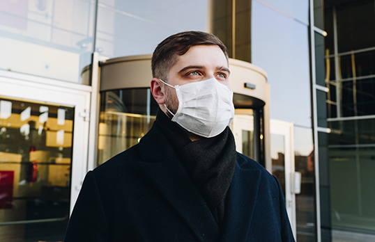 Man stands outside building in a face mask